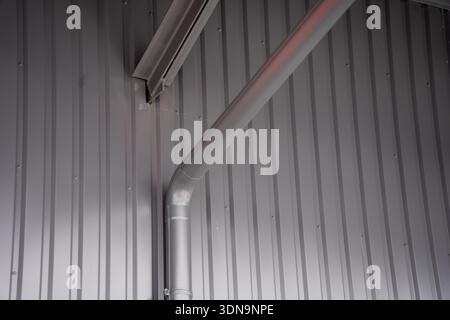 Vue intérieure du mur en métal ondulé gris avec tuyau de conduit de ventilation incliné et connexion de poutre structurelle, montrant la construction de bâtiments industriels Banque D'Images
