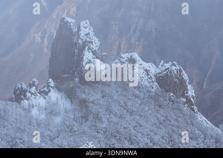 Spectaculaire vue hivernale des flèches Grignetta émergeant d'un épais brouillard et de nuages bas. Paysage alpin Moody avec des sommets rocheux enneigés dans les montagnes Banque D'Images