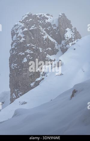 Spectaculaire vue hivernale des flèches Grignetta émergeant d'un épais brouillard et de nuages bas. Paysage alpin Moody avec des sommets rocheux enneigés dans les montagnes Banque D'Images