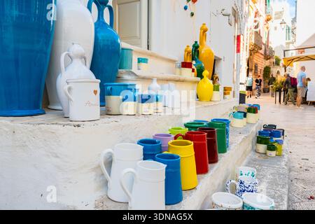 LOCOROTONDO, POUILLES - OCT 11, 2025 : vases et tasses en céramique vibrants aux couleurs arc-en-ciel affichés sur des marches en pierre blanche dans la ville de Locorotondo, Pouilles, Italie Banque D'Images