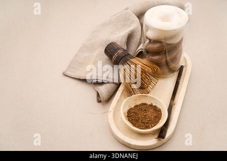 Hojicha latte sur un plateau avec de la poudre de thé et un fouet en bambou Banque D'Images