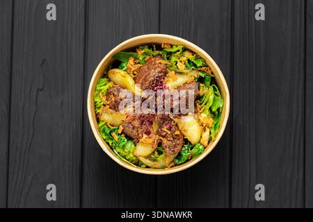 Salade de foie chaude avec poire caramélisée, légumes verts mélangés et oignons croustillants dans un bol kraft Banque D'Images
