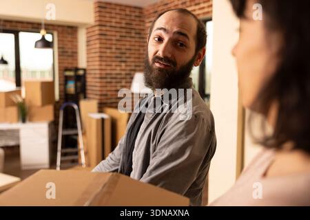 Homme blanc barbu avec petite amie arrivant à la maison récemment achetée, tenant des boîtes en carton et entrant dans un nouvel espace de vie. Couple caucasien emménageant avec des affaires emballées. Banque D'Images