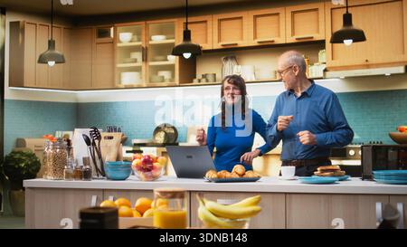 Des personnes âgées ludiques dansant dans la cuisine et profitant de la musique du matin. Mouvements groovy et goofy montrant la passion romantique, le bonheur et la beauté d'une relation amoureuse à la maison. Caméra A. Banque D'Images