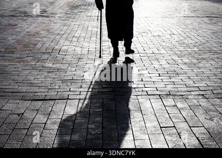 Silhouette et ombre de femme marchant avec une canne sur la rue de la ville en hiver. Concept de boiterie, handicap, vieillesse, maladies de la colonne vertébrale Banque D'Images