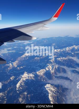 Blick aus dem Flugzeugfenster : Passagierflugzeug im Flug über den verschneiten Gipfeln der Alpen Banque D'Images
