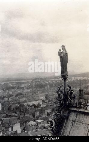 Une statue sur le toit d'une figure rooftop tenant un enfant se dresse sur un piédestal orné surplombant le tissu urbain dense ci-dessous. La base sculptée et la position élevée soulignent sa présence sculpturale, tandis que les rangées de toits s'étendent au loin. Cette vue surélevée de 1927 capture Clermont‑Ferrand vue d'en haut. D'une collection de photographies uniques du XXe siècle. Photographe amateur, clichés et quelques-uns plus grands dans un seul album, retraçant les voyages européens d'une famille. Banque D'Images