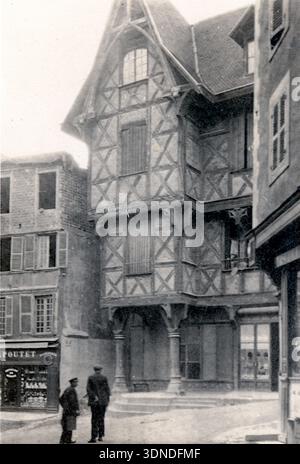 Un grand bâtiment à colombages se dresse au coin de la rue, ses étages supérieurs en surplomb soutenus par des poteaux en bois et des poutres à motifs. Des fenêtres à volets bordent la façade tandis que trois personnes conversent en dessous. Les devantures de magasins voisines encadrent la scène, capturant le caractère du début du siècle de Thiers et son architecture urbaine traditionnelle. D'une collection de photographies uniques du XXe siècle. Photographe amateur, clichés et quelques-uns plus grands dans un seul album, retraçant les voyages européens d'une famille. Banque D'Images