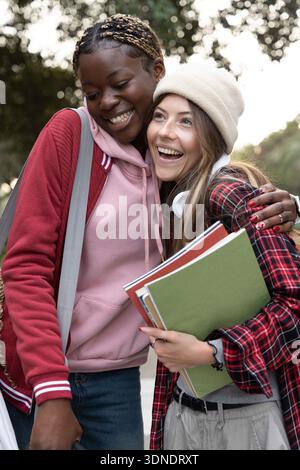 Étudiantes adolescentes diverses debout sur un chemin bordé d'arbres, penchées et souriantes, tenant des cahiers Banque D'Images
