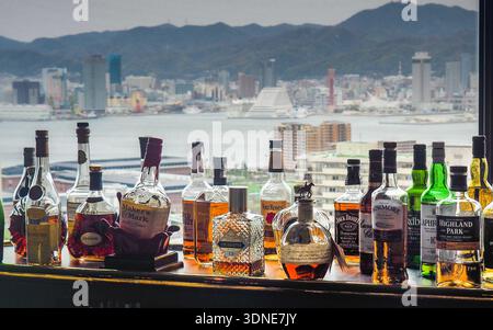 Bouteilles de whisky sur le comptoir du bar avec la tour de Kobe floue et l'horizon de la ville floue en arrière-plan. Banque D'Images