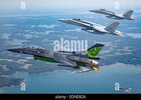 La photographie montre un F-16AM de l'armée de l'air belge combattant Falcon dans la livrée Dream Viper volant air-air avec des chasseurs F/A-18C Hornet de l'armée de l'air suisse pendant le Turku Airshow 2023. Le F-16AM est un réacteur monomoteur multirôle propulsé par un turboréacteur Pratt and Whitney F100-PW-220. Le F/A-18C Hornet est un chasseur bimoteur utilisant deux turboventilateurs General Electric F404-GE-402. La formation rapprochée met en évidence les manœuvres acrobatiques, la perspective du pilote et les marquages militaires détaillés. Banque D'Images