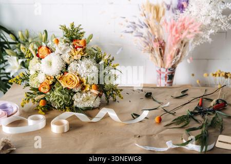 Bouquet de fleurs avec des roses et des chrysanthèmes se trouve sur du papier brun près de rouleaux de ruban. Floraison durable, emballage cadeau sans plastique Banque D'Images