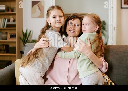 Femme d'âge moyen embrassant deux filles à l'intérieur souriant Banque D'Images
