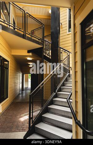 Escalier moderne contemporain avec mains courantes en métal menant dans un bâtiment résidentiel avec extérieur jaune. Les escaliers sont en métal inoxydable. Banque D'Images