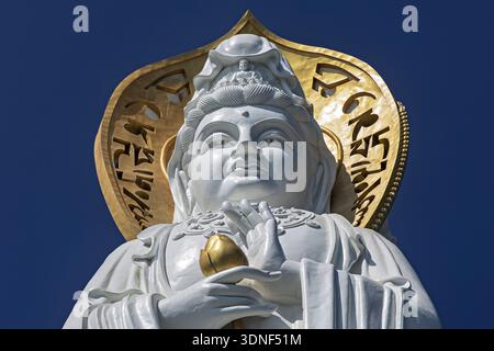 Vue d'une statue blanche immaculée de Guanyin à Nanshan, encadrée par un halo doré rayonnant et une écriture complexe, contre un ciel bleu Azur profond, Sanya, Chine. Banque D'Images