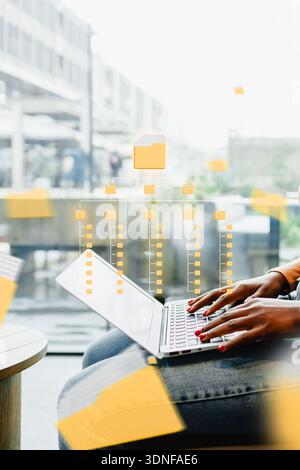 Personne utilisant un ordinateur portable dans un espace de travail moderne avec des superpositions numériques pour l'analyse du flux de données Banque D'Images