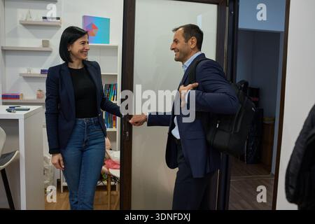 Femme d'affaires accueillant homme d'âge moyen en costume à la porte du bureau avec des sourires amicaux Banque D'Images