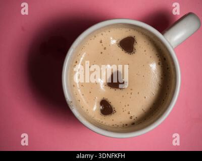 Tasse chaude de café cappuccino avec des coeurs d'amour au chocolat sur fond rose Banque D'Images