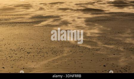 Vent soufflant du sable sur une plage créant des motifs et de la texture dans une lumière dorée Banque D'Images