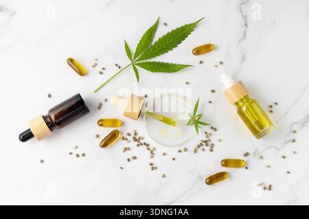 Huile de CBD dans des bouteilles en verre pipette et compte-gouttes, capsules de graines de chanvre médical sur fond de table en marbre avec feuille de plante de cannabis. Produits de cannabis Banque D'Images