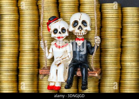 Figurines squelette de mariée et mariée assis sur une balançoire devant des pièces d'or empilées, symbolisant l'amour, la richesse, l'héritage et le destin financier Banque D'Images