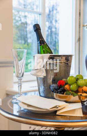 Élégante bouteille de champagne posée dans un seau à glace givré à côté d'une flûte en cristal et d'une assiette de fruits vibrante, créant une ambiance festive idéale pour les repas Banque D'Images