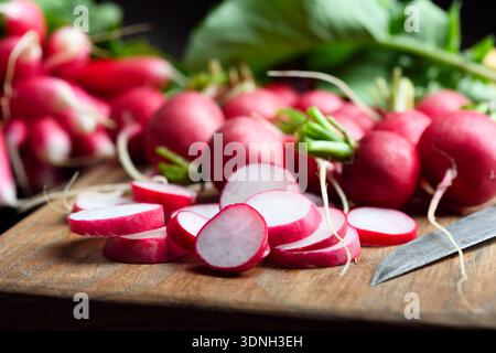 Gros plan de radis frais avec des dessus feuillus et des tranches sur une planche à découper. Légumes racines biologiques pour les repas de détox et la cuisine de la ferme à la table Banque D'Images