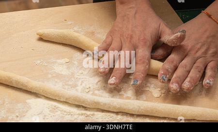 Les mains saupoudrées de farine roulent la pâte fraîche en brins lisses, capturant un moment tranquille et artisanal de pâtes maison, de tradition et de la beauté tactile de s. Banque D'Images