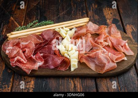 Plateau de charcuterie gastronomique composé de salumi italien, de cubes de fromage, d'olives et de gressins disposés sur un fond en bois Banque D'Images