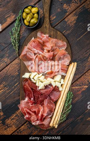 Plateau de charcuterie gastronomique composé de salumi italien, de cubes de fromage, d'olives et de gressins disposés sur un fond en bois. Banque D'Images