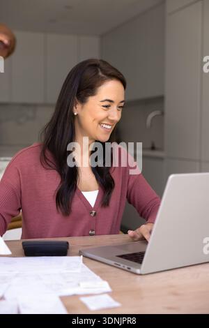 Femme souriante gérant des factures à l'aide d'un ordinateur portable à la maison Banque D'Images