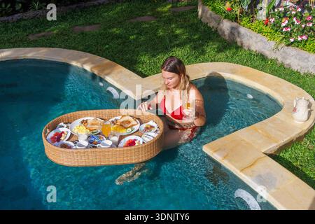 Jeune femme appréciant le petit déjeuner flottant dans la piscine privée à Luxury Bali Villa Banque D'Images