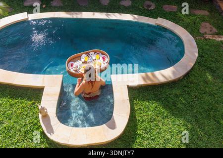 Jeune femme appréciant le petit déjeuner flottant dans la piscine privée à Luxury Bali Villa Banque D'Images