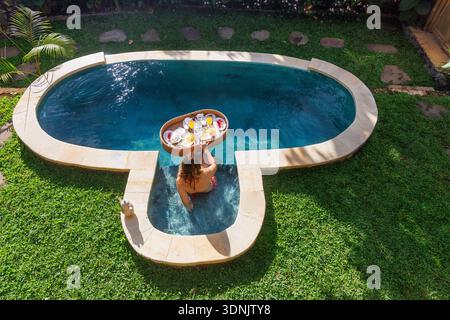 Jeune femme appréciant le petit déjeuner flottant dans la piscine privée à Luxury Bali Villa Banque D'Images