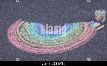 Arc-en-ciel coloré dessiné à la craie sur un pavé d'asphalte avec un seau de crayons. Banque D'Images