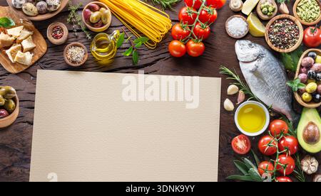 Assortiment de nourriture méditerranéenne sur une table en bois rustique. Le papier blanc au centre fournit un espace de copie pour les recettes, les menus ou les concepts alimentaires. Banque D'Images