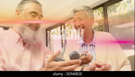 Vérifier le couple mature tenant la jauge de pression artérielle sur le canapé du salon dans une chemise rose et un cardigan Banque D'Images