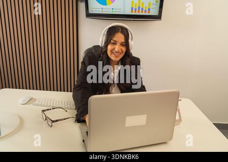 Femme d'affaires travaillant à distance, participant à une réunion en ligne avec écouteurs et ordinateur portable Banque D'Images
