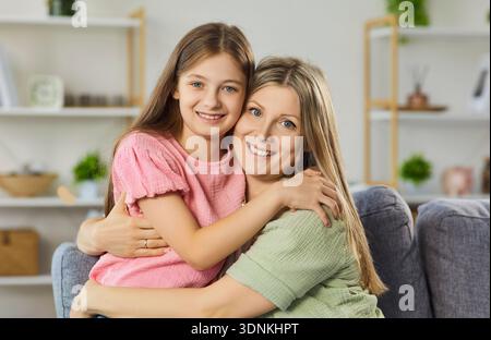 Mère heureuse embrassant sa fille à la maison, liens étroits et émotions positives Banque D'Images