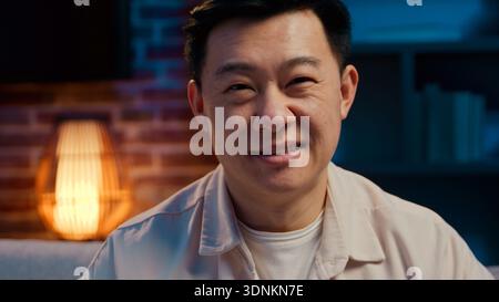 Portrait heureux souriant joyeux homme asiatique d'âge moyen dans la nuit soir à la maison regardant la caméra visage insouciant d'adulte chinois ethnique japonais coréen Banque D'Images