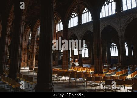 Vue large sur l'intérieur d'une église gothique avec des rangées de chaises vides éclairées par la lumière douce du jour à travers de grandes fenêtres cintrées. Banque D'Images