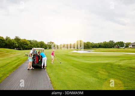 Couple d'amis, voiturette de golf et sac au cours avec équipement, espace et ciel pour le transport sur fairway. Personnes, groupe et extérieur avec équipement sportif Banque D'Images