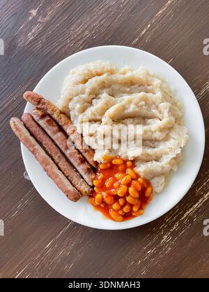 Vue de dessus montre assiette avec saucisses, haricots dans la sauce tomate, purée de pommes de terre sur la table en bois. Repas maison copieux avec combinaison de plats de confort classique Banque D'Images