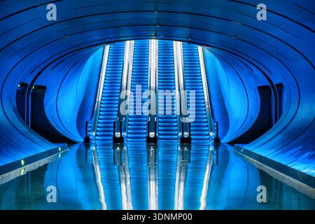 Escaliers futuristes éclairés bleus à l'intérieur d'une station de métro moderne avec une architecture de tunnel incurvée et un sol réfléchissant. Symétrie, minimalisme Banque D'Images