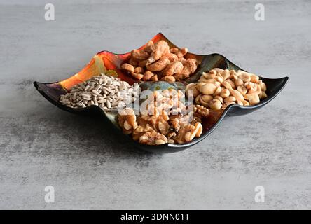 Trois types de noix (noix, arachide, noix de cajou) et graines de tournesol dans un bol coloré sur un fond gris Banque D'Images