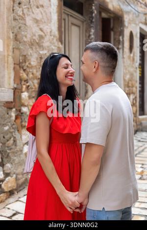 Couple souriant tenant la main sur la vieille rue. Heureux couple se tenant la main et souriant l'un à l'autre sur une rue pavée étroite dans un charmant historique Banque D'Images
