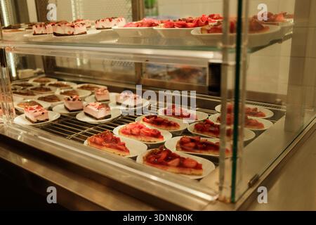 Tranches de cheesecake à la fraise disposées sur des assiettes à l'intérieur d'une vitrine de boulangerie. Concept de dessert de fruits frais pour le menu de café et vitrine de pâtisserie. Banque D'Images
