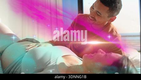 Homme souriant touchant une femme enceinte portant un débardeur sur le lit près de la fenêtre, recouvrement turquoise magenta Banque D'Images