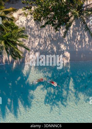 Les couples profitent d'une journée paisible flottant dans des hamacs sur des eaux turquoises claires à Bang Bao Beach. Le soleil projette de belles ombres des palmiers qui se balancent, créant une scène tropicale parfaite. Banque D'Images