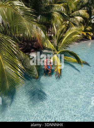 Un couple aimant profite d'un moment romantique dans les eaux sereines de la plage de Khlong Hin à Koh Kood, en Thaïlande. Les palmiers verdoyants créent une atmosphère paradisiaque tropicale. Banque D'Images